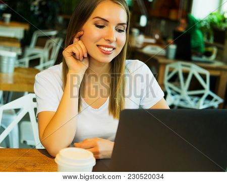 Happy young woman drinking coffee/tea and using laptop  in a cof