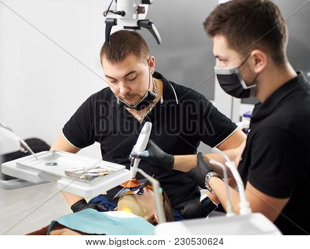 Stomatologist Looks At The Patient While His Assistant Is Completing The Process Of Filling The Toot