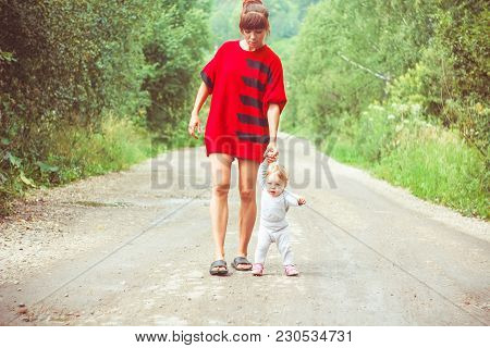 The Child Learns To Walk In The Park Barefoot On The Grass