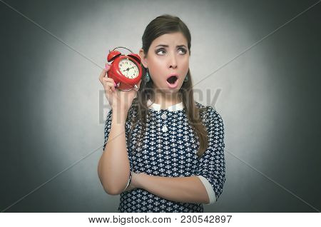 Sleepy Woman Holding In Hands Alarm Clock And Looking Aside. Latecomer Student Or Emloyee. Be Late A