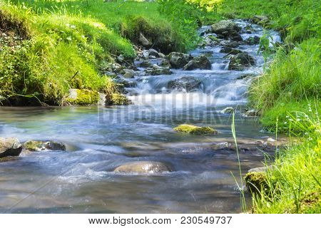 Rocky Mountain Stream With Green Vegetation On Both Sides