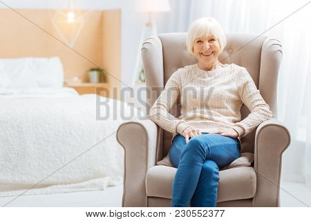 Comfort. Cute Pleasant Aged Lady Feeling Good While Being Alone In A Beautiful Light Room And Sittin