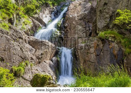 Waterfall Of A Small Stream On The Cliff Side, With Green Vegetation.
