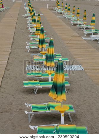 Yellow And Green Beach Chairs And Umbrellas Arranged Along An Italian Beach