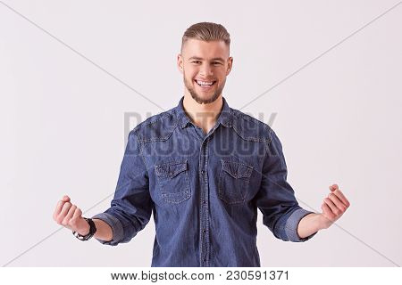 Portrait of happy young man in denim shirt gesturing and smiling while isolated on white background. Stylish bearded hipster man expressing positive emotions. Handsome man winner celebrating victory