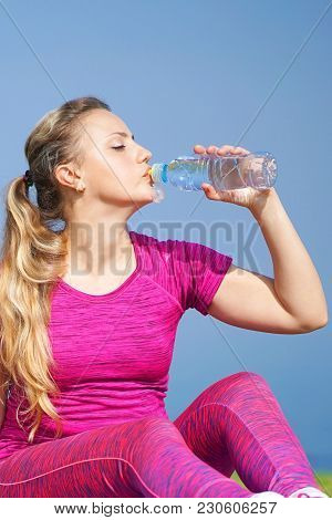 Side View Of Beautiful Girl In Sport Clothes Drinking Water After Workout On The Beach. Young Woman 