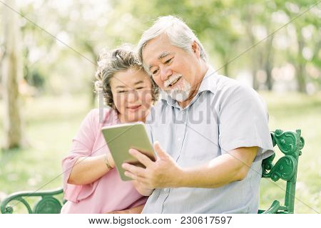 Happy And Smile Senior Asian Couple Using Digital Tablet Together Outdoor In Park