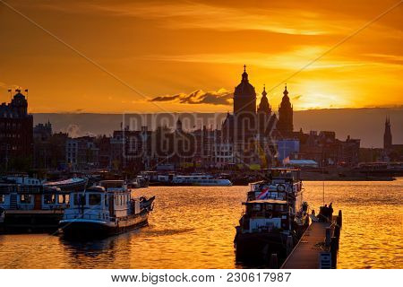 Amsterdam cityscape skyline with Church of Saint Nicholas (Sint-Nicolaaskerk) and boats on the pier on sunset with dramatic sky. Amsterdam, Netherlands