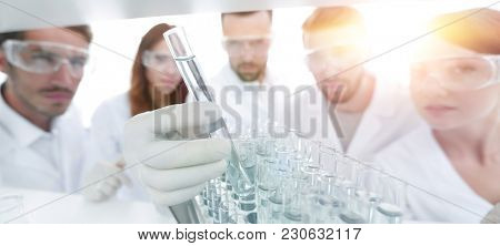 background image is a group of microbiologists studying the liqu