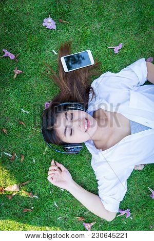 Young Woman Lying On Grass Floor Listening Music From Moblie Phone With Headset. Girl Chilling Lifes