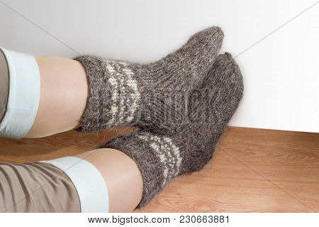 Pair Of The Thick Gray Wool Hand-knitted Socks On Women Legs On The Wooden Floor On A Light Colored 