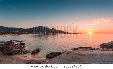 Sun Setting On Rocky Outcrops And Sandy Beach At Algajola In The Balagne Region Of Corsica