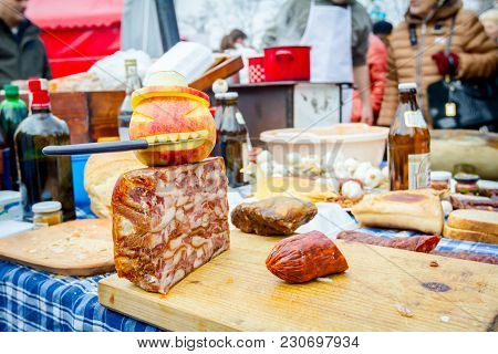 Headcheese And Smoked Sausage On A Wooden Chopping Board At Outdoor Kitchen, People In Background Ar