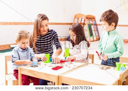 Babysitter And Children Play With Kinetic Sand In The Daycare