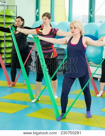 Women Doing Exercise With Latex Fitness Band During Workout In A Gym.