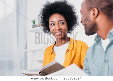 African American Couple Holding Books And Looking At Each Other At Home
