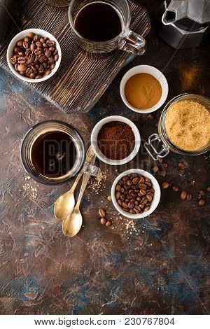 Coffee In Glass Cup, Coffee Beans, Ground Coffee And Brown Cane Sugar On Dark Background