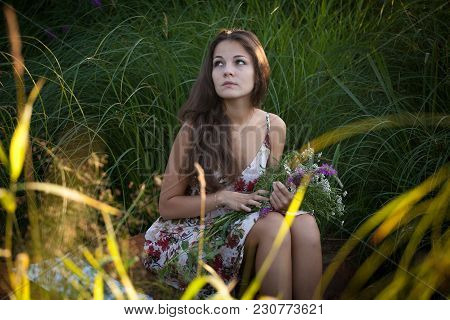 The Young Beautiful Girl, With A Bouquet Of Flowers, Has A Rest And Enjoys Beauty Of The Nature In T