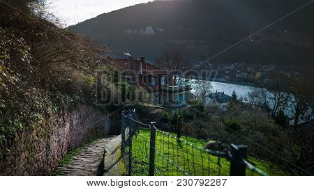 Beautiful View From The Hill At The Cityscape And River. Scenic Stone Road Leading Down. Sun Rays Ar