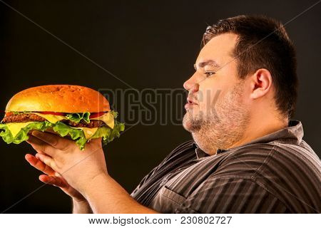 Man eating fast food hamberger. Fat person made great huge hamburger and admires him, intending to eat it. Junk meal leads to obesity. Health problems due to malnutrition.