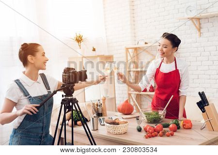 Two Culinary Bloggers In Red Aprons Tasting Winewith One Girl Behind Camera.