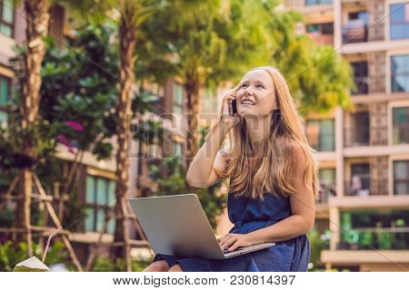 Young Female Freelancer Sitting Near The Pool With Her Laptop In The Hotel Browsing In Her Smartphon