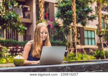Young Female Freelancer Sitting Near The Pool With Her Laptop In The Hotel Browsing In Her Smartphon