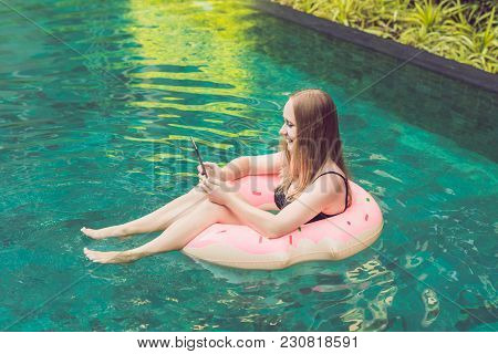 Young Female Freelancer Sitting Near The Pool With Her Laptop In The Hotel Browsing In Her Smartphon