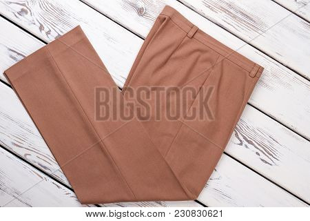 Folded Brown Trousers. V-shape Of Unisex Pants, Bright Beige Wooden Desks Surface Background.