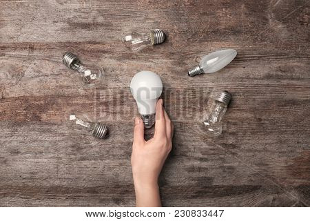 Woman holding LED lamp near incandescent light bulbs on wooden background