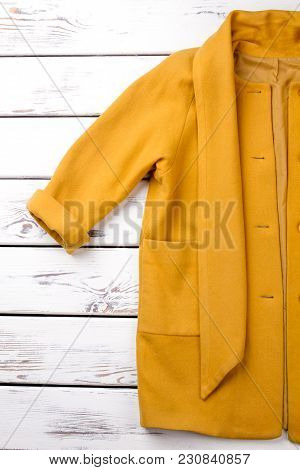 Rolled Up Yellow Coat Sleeve. Cropped Vertical View. White Desk Wooden Background.