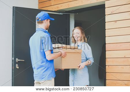 Smiling delivery man in blue uniform delivering parcel box to recipient - courier service concept. Smiling delivery man in blue uniform