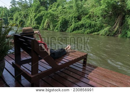 Asian Girl In The Resort In Red Clothes And Hat Sleep On Bed Pool., Background Of A Beautiful River.