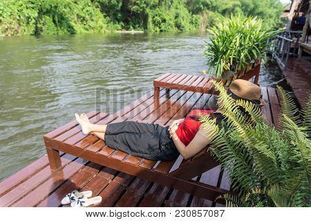 Asian Girl In The Resort In Red Clothes And Hat Sleep On Bed Pool., Background Of A Beautiful River.