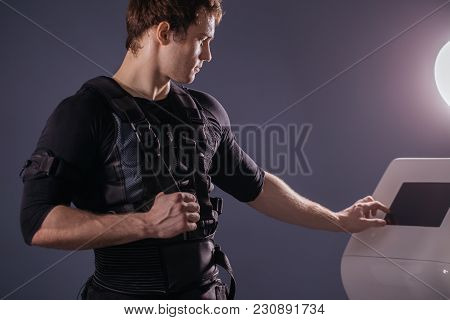 Male Athlete Regulating Intensity Of Ems Electro Muscular Stimulation Machine