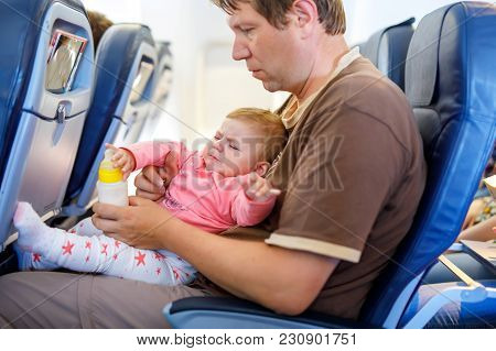 Young Sad Tired Father And His Crying Baby Daughter During Flight On Airplane Going On Vacations. Da