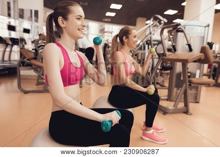 Mother And Daughter In Sportswear Sitting Doing Exercises With Dumbbells At The Gym. They Look Happy