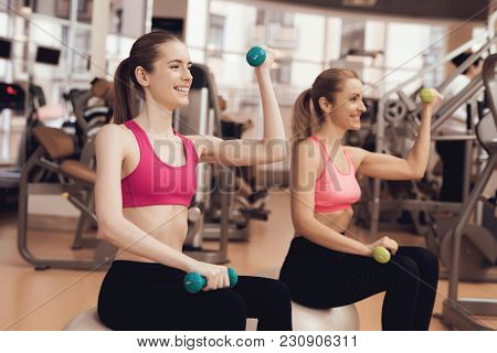 Two Women In Sportswear Sitting Doing Exercises With Dumbbells At The Gym. They Look Happy, Fashiona