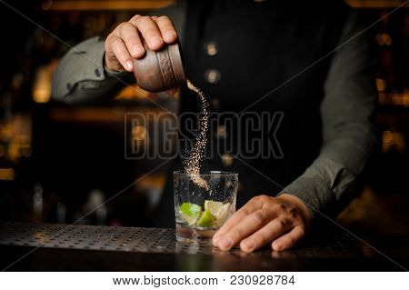 Barman Pouring Cane Sugar Into The Cocktail Glass With Slices Of Lime On The Bar Counter