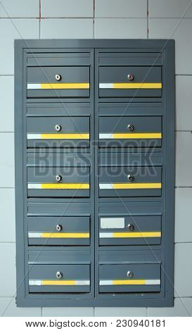 Grey Steel Modern Lockable Mailboxes In A Tiled Exterior Wall With Yellow And White Labels
