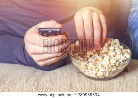 A Man With A Bowl Of Popcorn And A Remote Control In His Hand Looks At The Tv On The Sofa