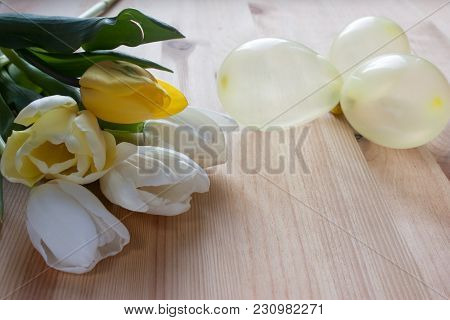 Three White Tulips, Two Yellow Tulips And Three Yellow Little Air Balloons On A Light Wooden Backgro
