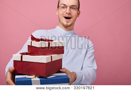 A Surprised Man In Shirt With Glasses Holds Gifts In A Box With Lid And Red Bow In His Hands, Lookin