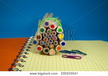 Pencil Crayon And Paperclips Lying On Wire Bound Open Notebook Ruled With Squares With Blue And Yell