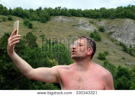 Adult Man In Glasses Holds A Smartphone In His Hand. A Traveler Blogger Takes A Selfie Or A Deaf-mut