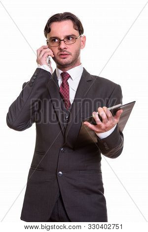 Thoughtful Young Businessman Talking On Mobile Phone While Holdi