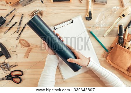 Female Carpenter Holding Diploma Certificate Tube Holder In Woodwork Workshop, Top View