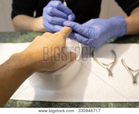Male Manicure. Woman Hands In Blue Sterile Gloves Holding Male Finger And Manicure Instrument Making