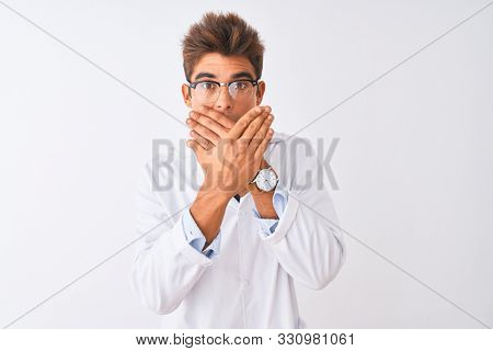 Young handsome sciencist man wearing glasses and coat over isolated white background shocked covering mouth with hands for mistake. Secret concept.