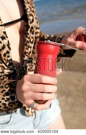 Red Manual Coffee Grinder In Female Hands Close Up. On Nature, Sea Background. Barista Girl